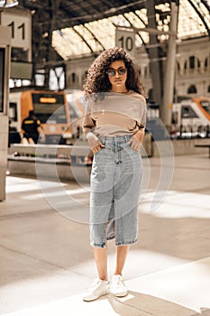 Fasionable young african model stands on railway station with hands in pockets in sunnny spring day.