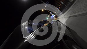 Fast black car driving at night road through the city, view from wheel. Footage. Modern vehicle moving along the busy