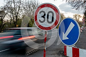 A fast driving blue speeding car with motion blur effect near the traffic sign limiting the maximum speed to 30 kph