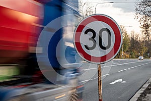 A fast driving blue speeding truck with motion blur effect near the traffic sign limiting the maximum speed to 30 kph