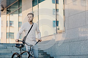 Fast eco city transport. Serious young guy in business clothes, walks with bike at city