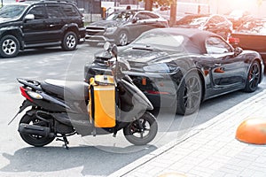 Fast express takeaway online gig order food delivery scooter with red orange bag box parked at traffic city center