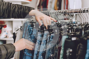 Fast fashion concept. Woman chooses jeans in a store. Lots of clothes in the store. Fast Fashion Destroying Planet