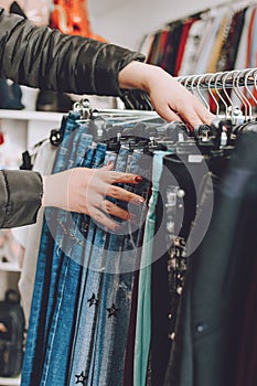 Fast fashion concept. Woman chooses jeans in a store. Lots of clothes in the store. Fast Fashion Destroying Planet