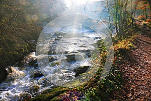 Fast flowing river, river path and sun streaks.