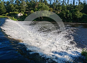 Fast flowing water cascading over dam on Ave River, Portugal