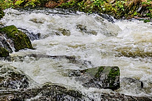 Fast flowing water stream between moss covered rocks of overflowing river photo