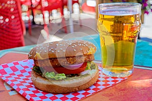 Fast food in bar served outdoor in sunny day, vegetarian hamburber and glass of cold beer