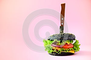 Fast food concept. Juicy black burger with knife on pink background. Take away meal. Unhealthy diet frame with copy space