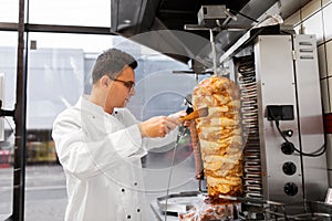 Chef slicing doner meat from spit at kebab shop