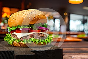 Fast food. Fresh beef burger with lettuce, tomato, cheese and onion, in a sesame bun, on a wooden board on the table, a