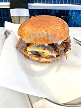 Fast Food Hamburger with Aioli Sauce, Cheddar Cheese, Mayonnaise and Bacon on White Burger Sheet / Street Food Cheeseburger