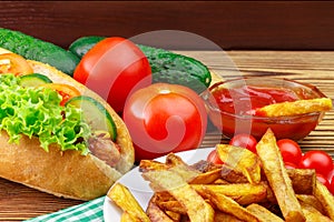Fast food meal, hot dog, french fries, ketchup, tomato and cucumber on wooden background.