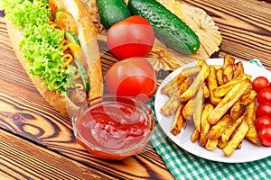 Fast food meal, hot dog, french fries, ketchup, tomato and cucumber on wooden background.