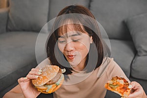 Fast food takeaway back home. Eating burger when takeout and delivery. Asian woman lifestyle in living room.