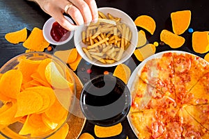 Fast food and unhealthy eating concept - close up of pizza,, french fries and potato chips and candies on wooden table top view