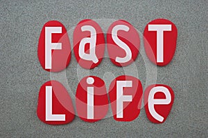 Fast life, creative slogan composed with red colored stone letters over green sand