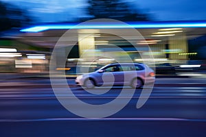 Fast-moving car in the street at night with blurred gas station on its background