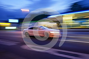 Fast-moving car in the street at night with blurred gas station on its background