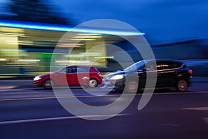 Fast-moving cars in the street at night with blurred gas station on their background