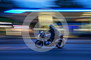 Fast-moving motorcycle in the street at night with blurred gas station on its background