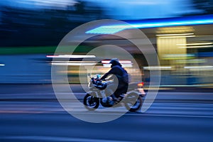 Fast-moving motorcycle in the street at night with blurred gas station on its background