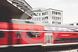 Fast moving red train at a railway station with white buildings in the background