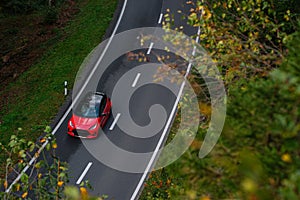 Fast moving red sport car with motion blur effect. Transport on a forest road in summer. Top view from above