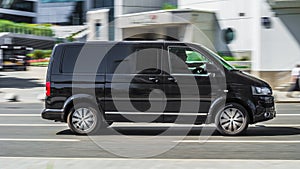 Fast moving Volkswagen Transporter T5 on the city road. Black minivan rides on street. Commercial auto in fast motion with blurred