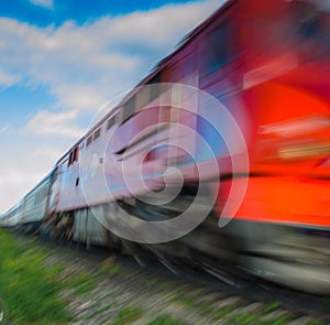 Fast passing nearby passenger train with motion blur effect against the evening sky with clouds. The concept of railway