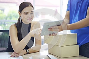 Fast and reliable service. Caucasian woman signing on tablet pc computer at home office. Delivery man brings delivering parcel box