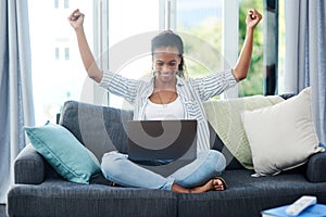 The fast wifi is working in her favor. Shot of a young woman cheering while using a laptop at home.