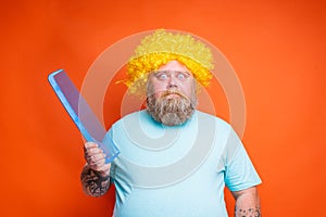 Fat amazed man with beard, tattoos and sunglasses combs himself with a giant comb