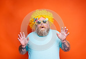 Fat amazed man with beard, tattoos and sunglasses has fun with the yellow wig