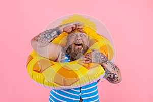 Fat amazed man with wig in head is ready to swim with a donut lifesaver