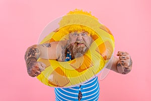 Fat angry man with wig in head is ready to swim with a donut lifesaver