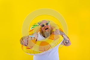 Fat annoyed man with wig in head is ready to swim with a donut lifesaver