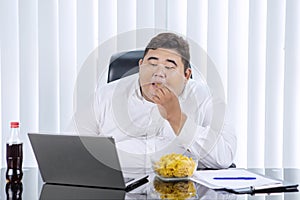 Fat Asian businessman eating chips while working