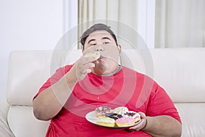 Fat Asian man eating doughnuts in his living room