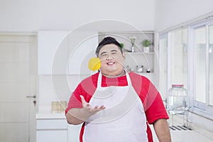 Fat Asian man flipping an orange in the kitchen