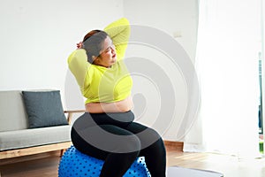 Fat Asian woman exercising at home, she sits on a yoga ball.