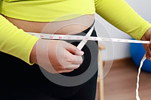 Fat Asian woman exercising at home using meter tape.