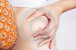 Fat burns with a pineapple diet. The woman squeezes the skin on her stomach, showing excess fat.