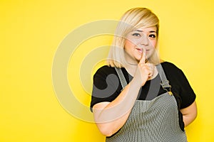 Fat Caucasian woman keeping a secret with a finger on her lips in a studio