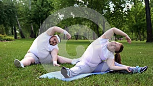 Fat couple having workouts in park together, beginners in weight loss program