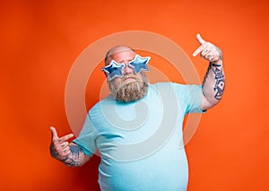 Fat delusion man with beard, tattoos and sunglasses is uncertain for something