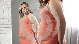 Fat female looking in mirror upset about her appearance, overweight insecurities