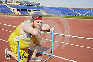 Fat funny man sitting down resting on the track in the stadium