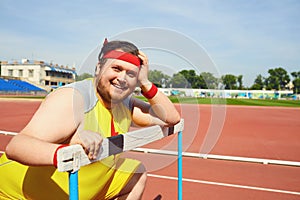 Fat funny man sitting down resting on the track in the stadium