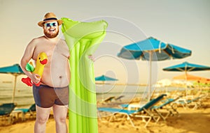 Fat funny man in swimming trunks with an inflatable mattress on a gray background.